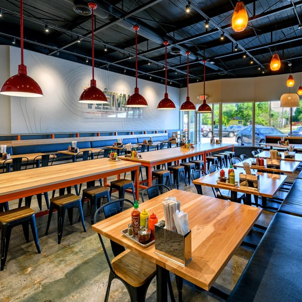 Spacious restaurant interior with light wood tables, dark blue booth seating, and red pendant lights.