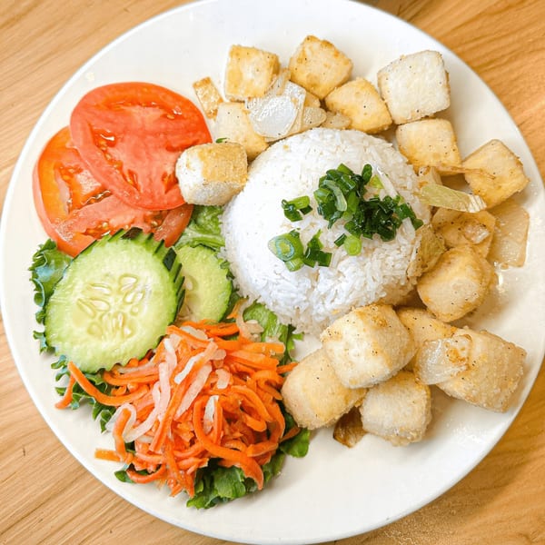 Vietnamese tofu and rice dish with sliced tomatoes, cucumbers, and shredded carrots on a white plate.