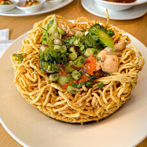 Crispy Vietnamese bird's nest noodles with chicken, broccoli, and fresh herbs on a white plate.