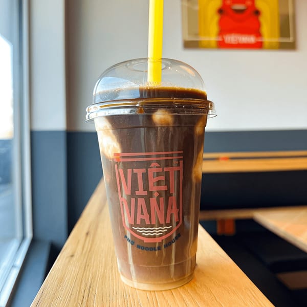 Vietvana Pho Noodle House iced coffee with a yellow straw on a wooden counter.