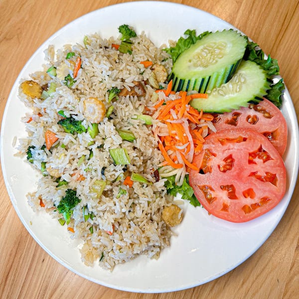 Vietnamese fried rice with vegetables, tofu, sliced cucumbers, tomatoes, and shredded carrots on a white plate.