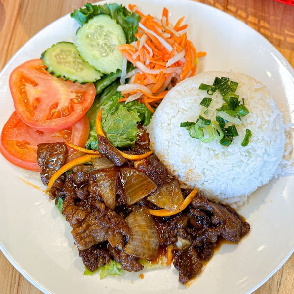 Vietnamese dish with beef, onions, rice, sliced tomatoes, cucumbers, and shredded carrots.