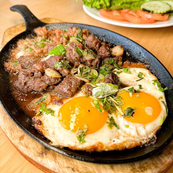 Sizzling Vietnamese beef and two fried eggs in a cast iron skillet, with a side salad.