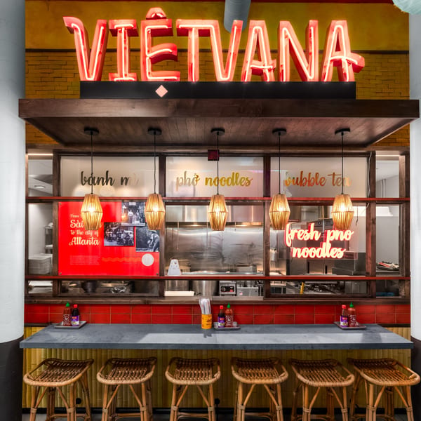 The interior of Vietvana restaurant, featuring a neon sign, counter seating, and an open kitchen.