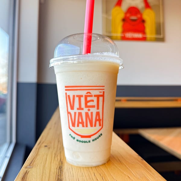 A Vietvana Pho Noodle House smoothie with a red straw on a wooden table.