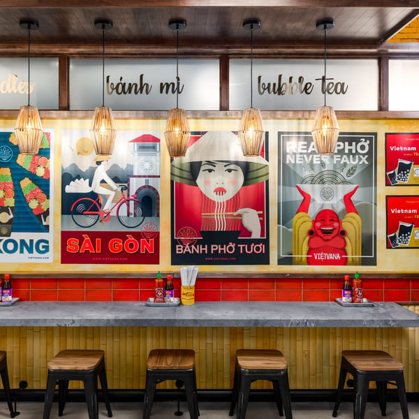A vibrant Vietnamese restaurant interior with a long counter, stools, and colorful posters on the wall.