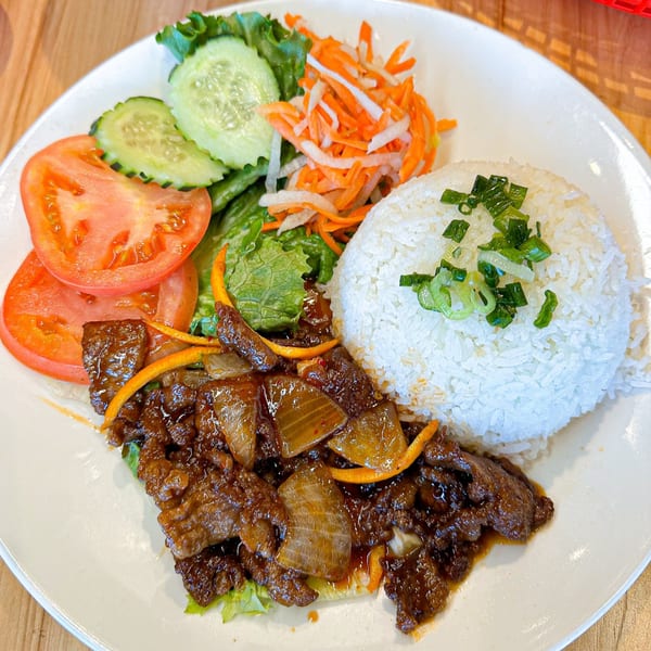 Vietnamese beef and onion stir-fry with white rice, sliced tomatoes, cucumbers, and pickled carrots.